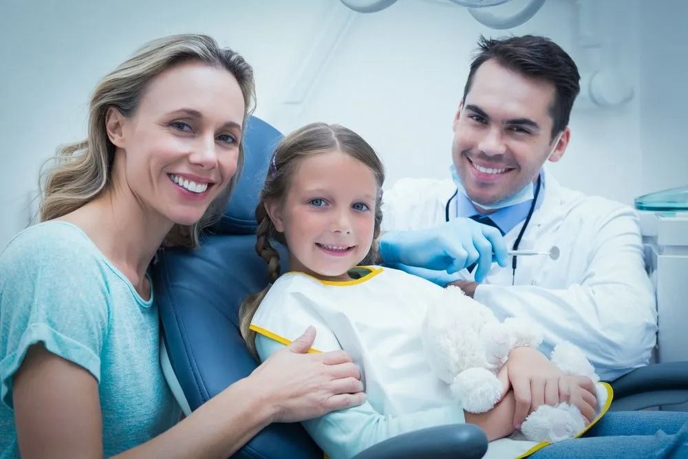 Woman, Child, and Dentist Smiling at the Camera in a Dentist's Office — Tamworth Orthocare In Narrabri, NSW