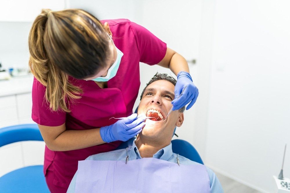 Dentist in Pink Scrubs Examining a Patient's Open Mouth — Tamworth Orthocare In Gunnedah, NSW