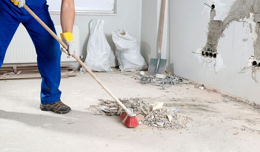 Worker using a pry bar to remove debris from a damaged concrete floor in a room under renovation