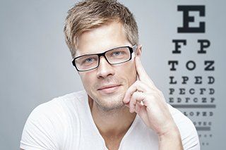 man in glasses seated in front of vision chart