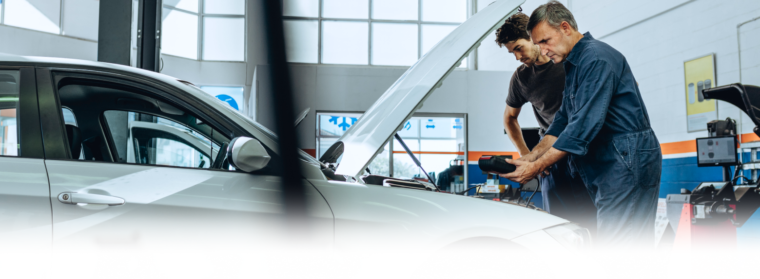 Two mechanics examining a car engine in an auto repair shop. The hood is open.