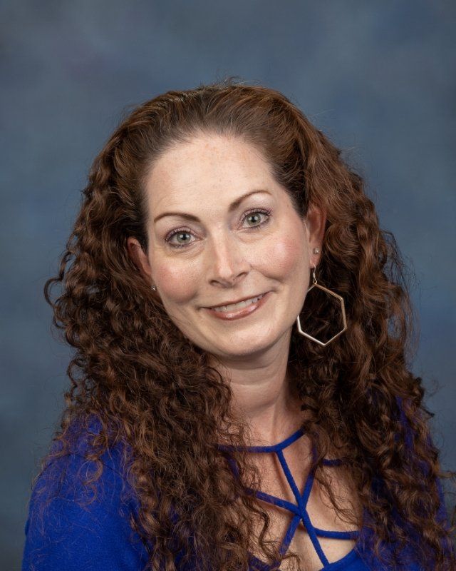 a woman with curly hair is wearing a blue shirt and earrings .