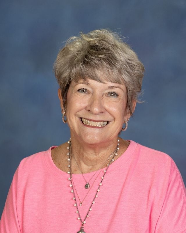 a woman in a blue floral shirt is smiling for the camera .