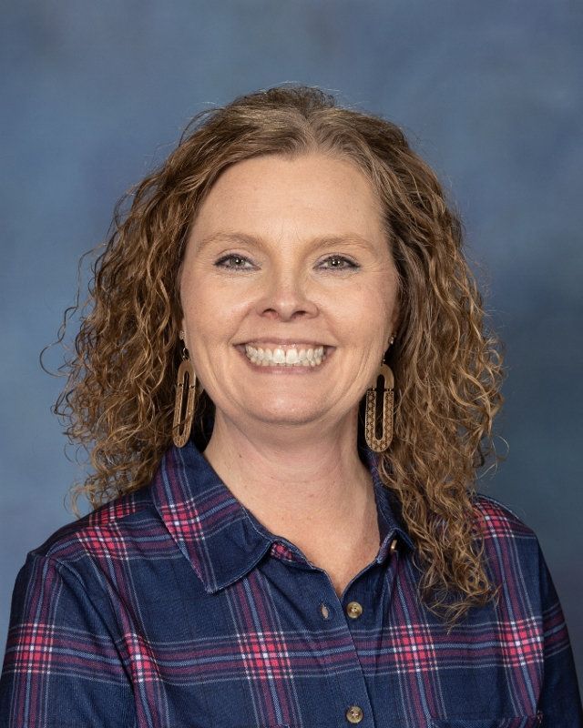 a woman with curly hair is wearing a plaid shirt and smiling for the camera .