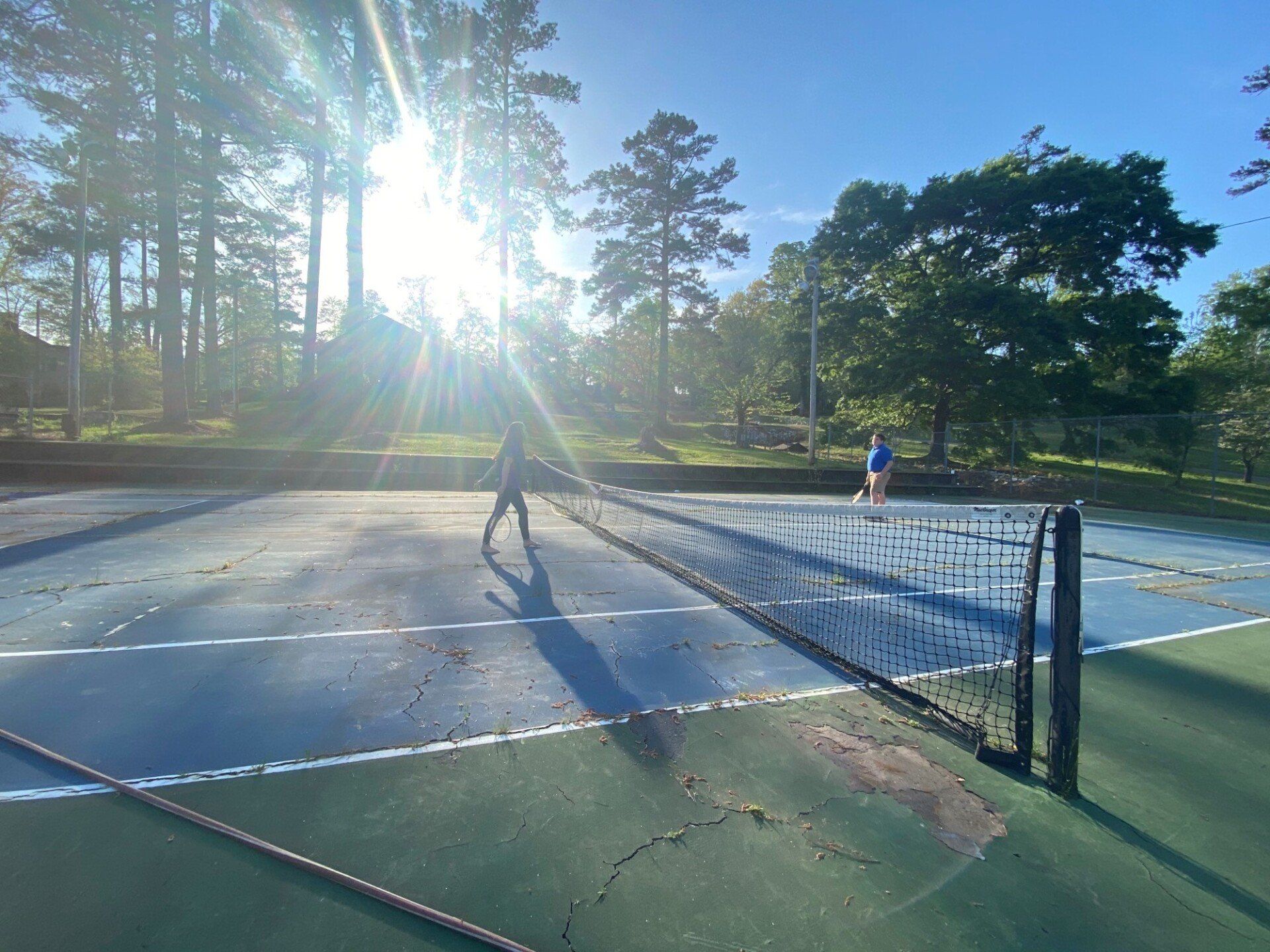 a person is playing tennis on a court with the sun shining through the trees