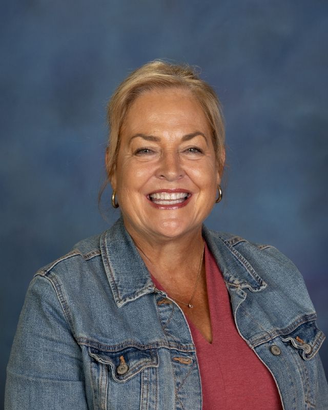 a woman wearing a white jacket and a satin blouse is smiling for the camera .