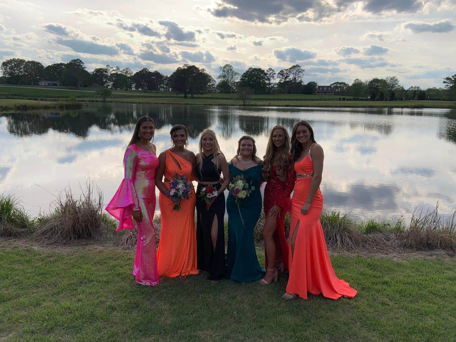a group of women in prom dresses are posing for a picture in front of a lake .