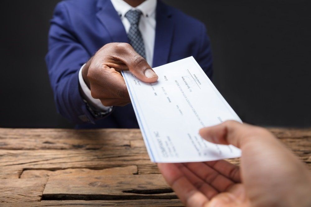 A man in a suit and tie is handing a check to another man.