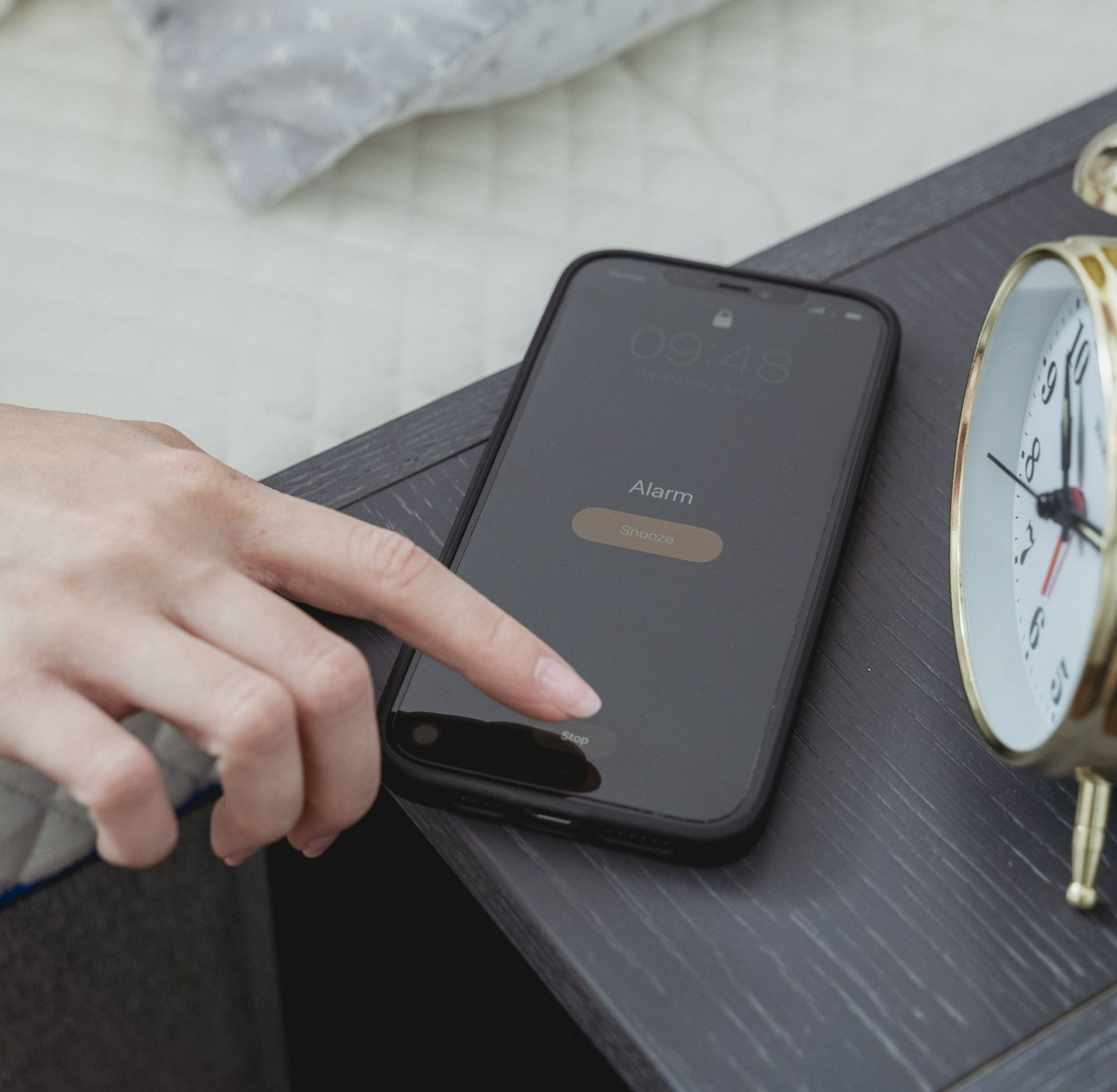 A person is pressing a button on a cell phone next to an alarm clock