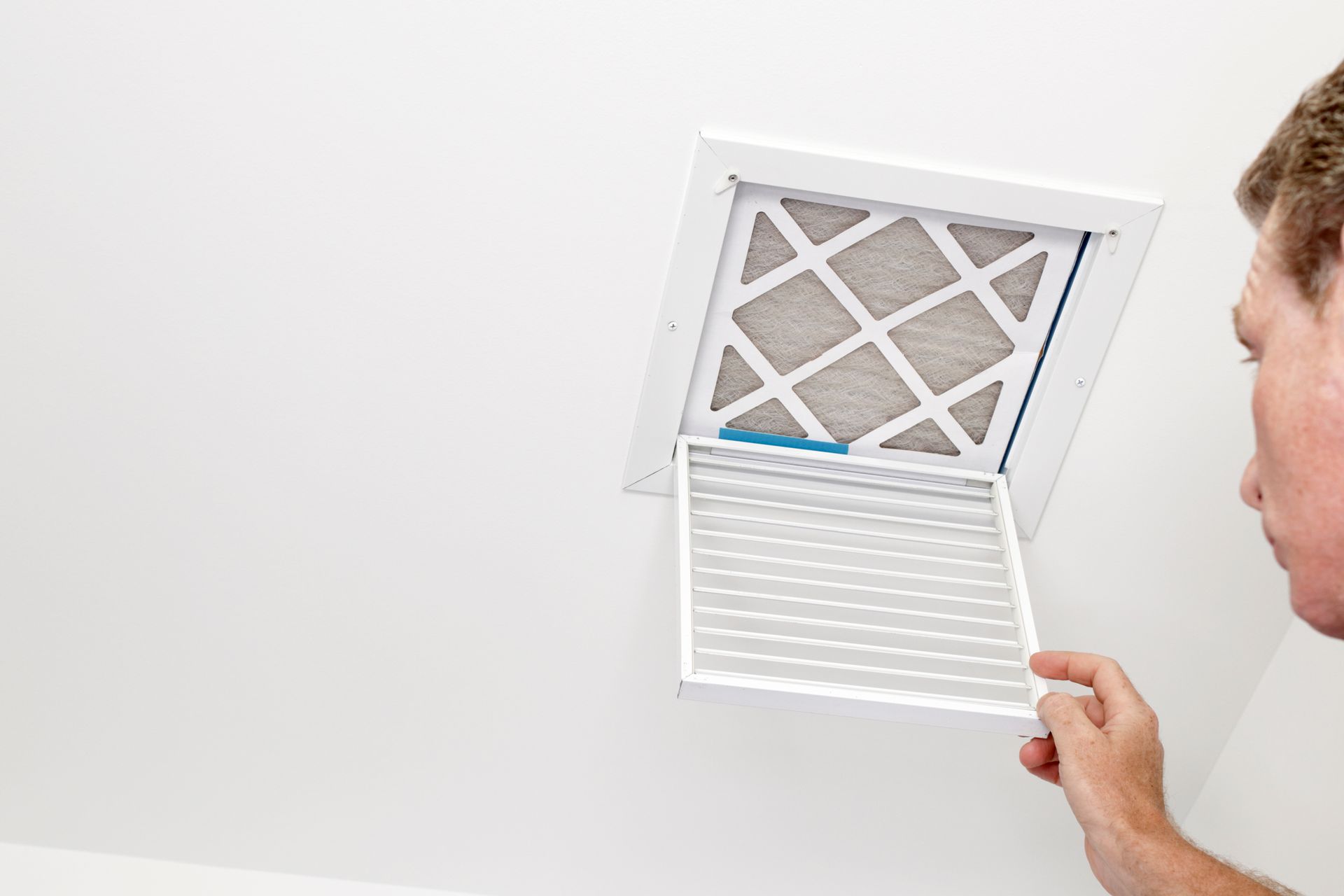 Man replacing an air filter in a white ceiling vent. The filter is dirty.