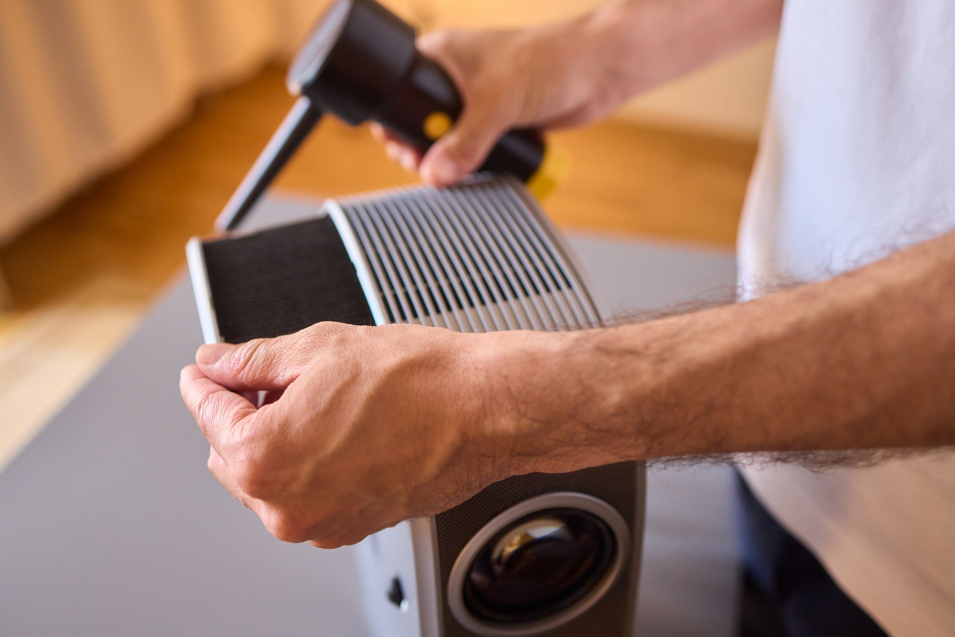 Person using a glue gun to repair a gray projector with silver vents.