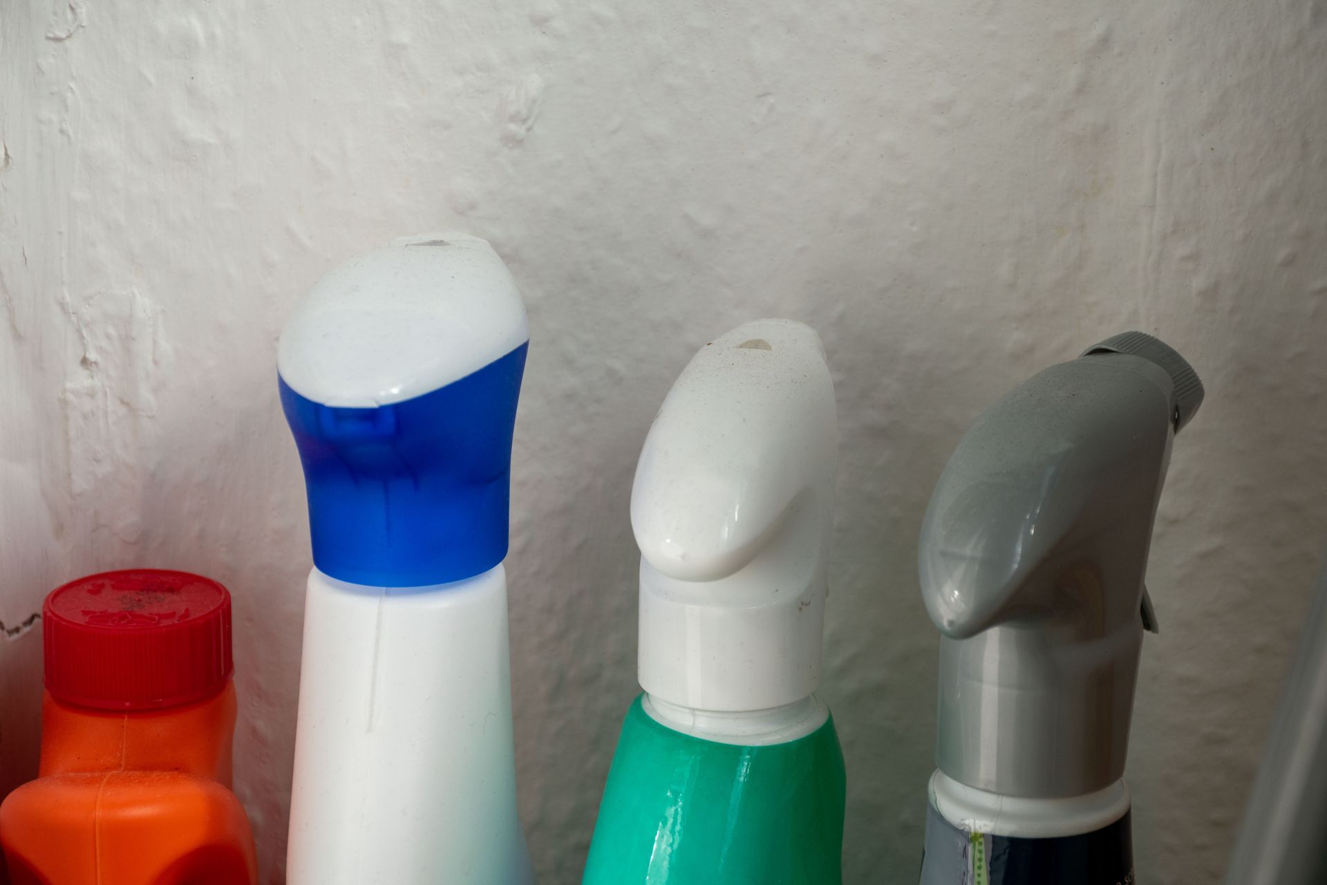 Close-up of four spray bottle tops, with red, blue, white, and gray colors, against a white wall.