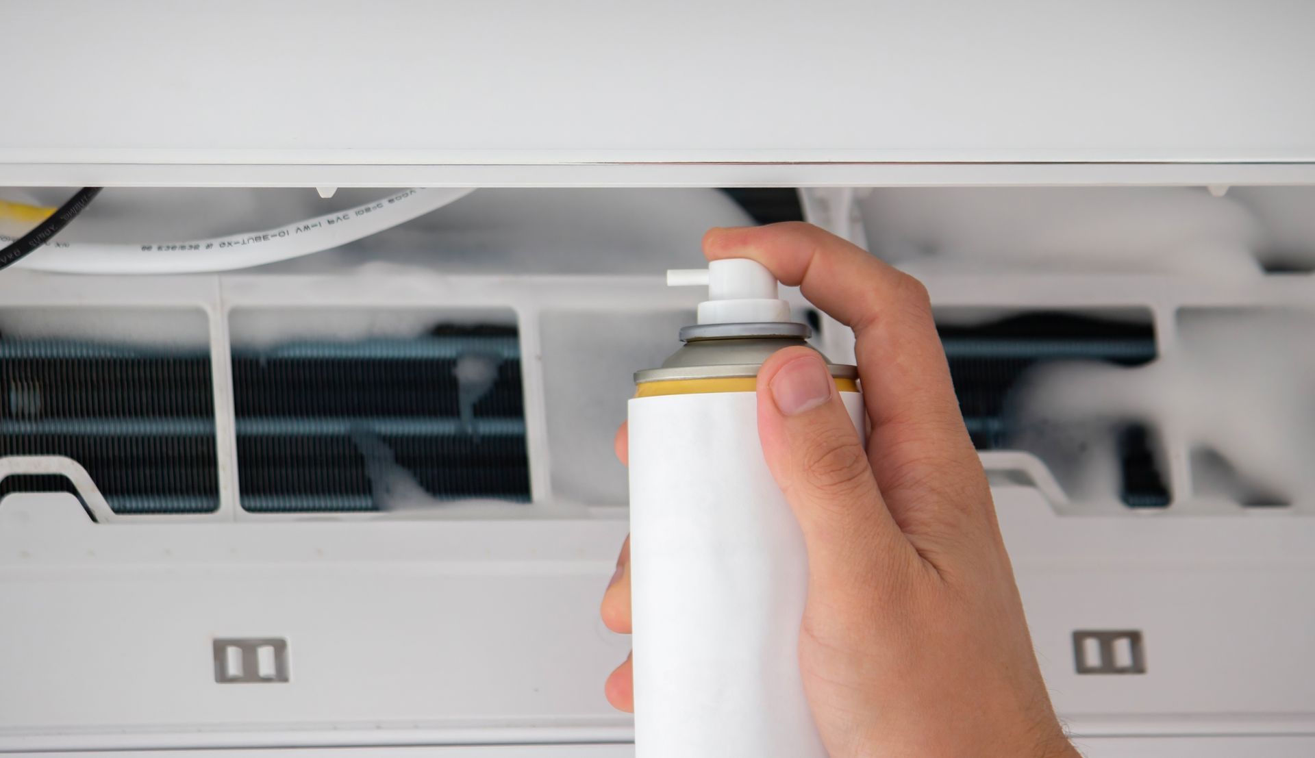 A person sprays cleaner into an open air conditioner unit.
