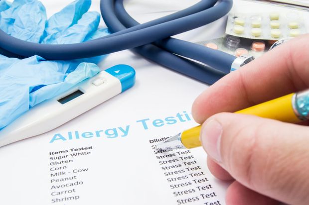Person marking allergy tests with a pen; stethoscope, gloves, thermometer, and pills in the background.
