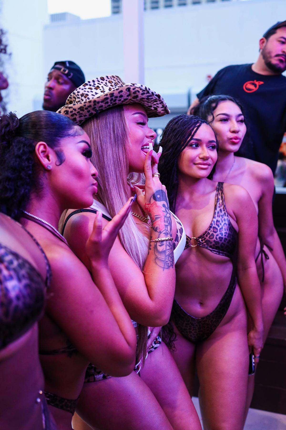 A group of people wearing leopard-print swimwear and a cowboy hat pose together at an indoor event with purple lighting.