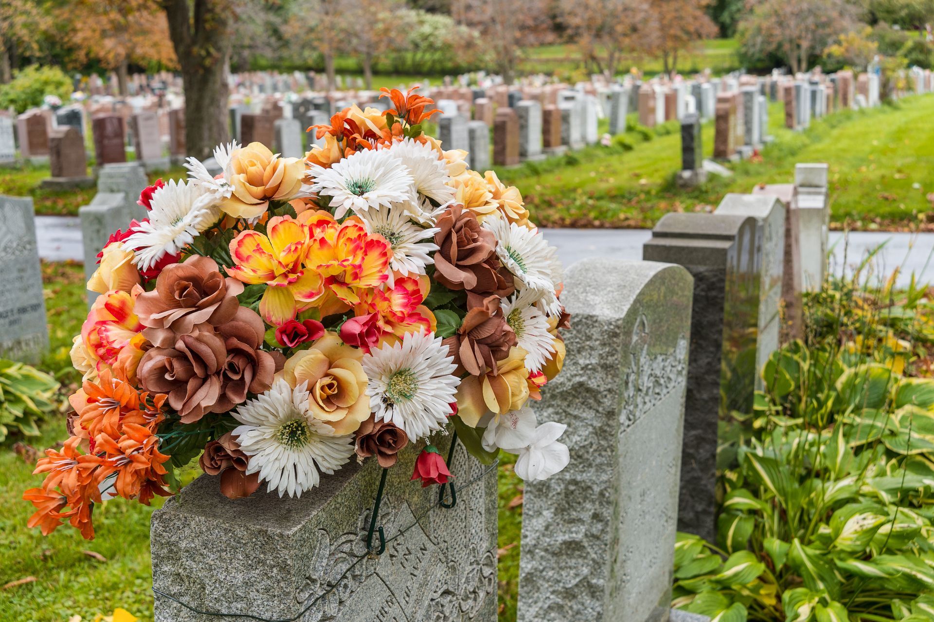 Close-up of colorful flowers on top of a cemetery tombstone, with more tombstones in the background. Close-up of colorful flowers on top of a cemetery tombstone, with more tombstones in the background.