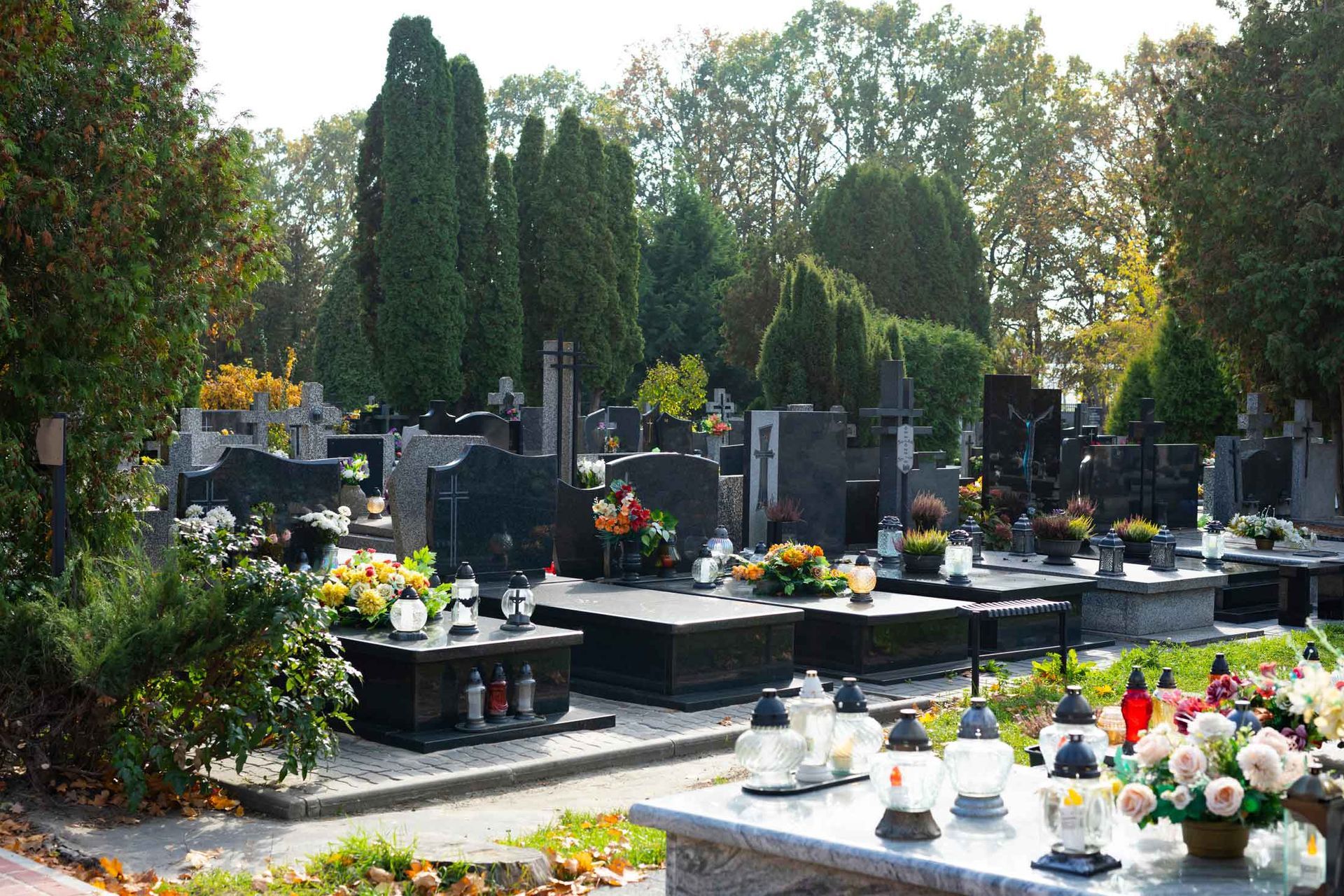 Tombstones decorated with flowers and grave candles at a cemetery surrounded by foliage.