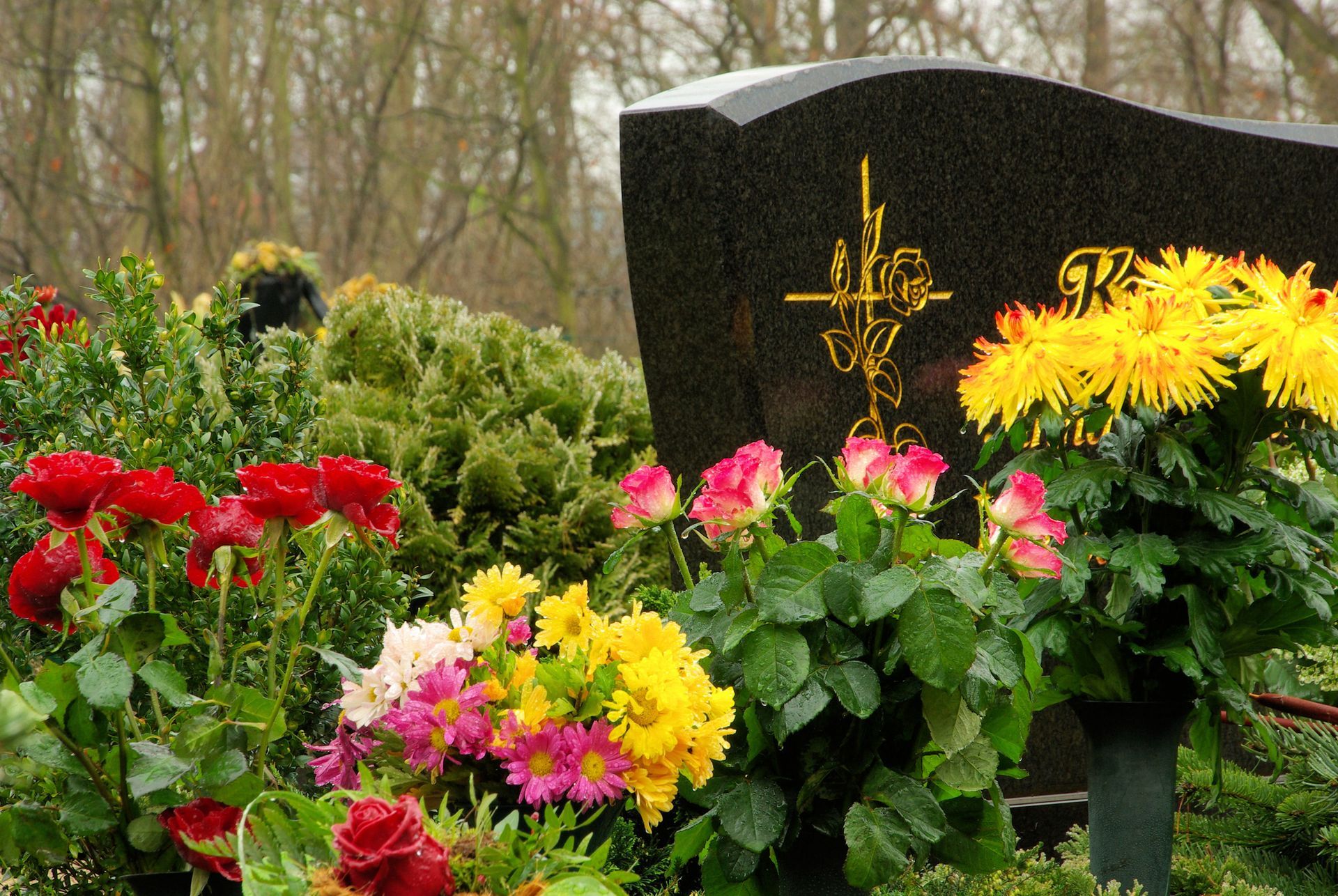 Black tombstone is covered with colorful and fresh floral arrangements. 