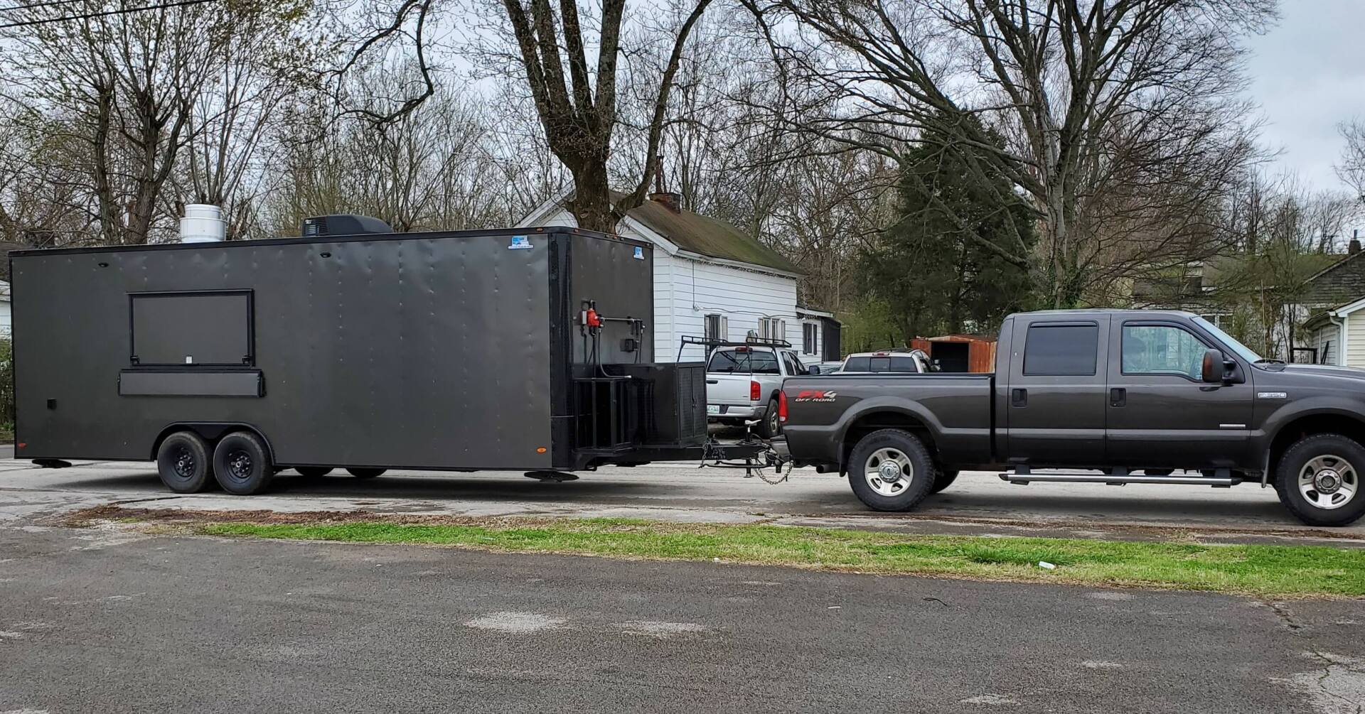A black truck is pulling a black trailer in a parking lot.