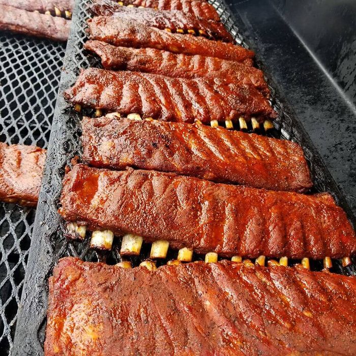 A row of ribs are cooking on a grill.