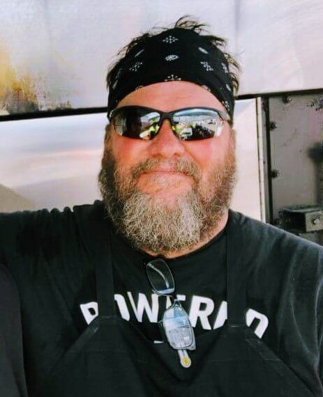 A man with a beard wearing sunglasses and a black shirt that says powered