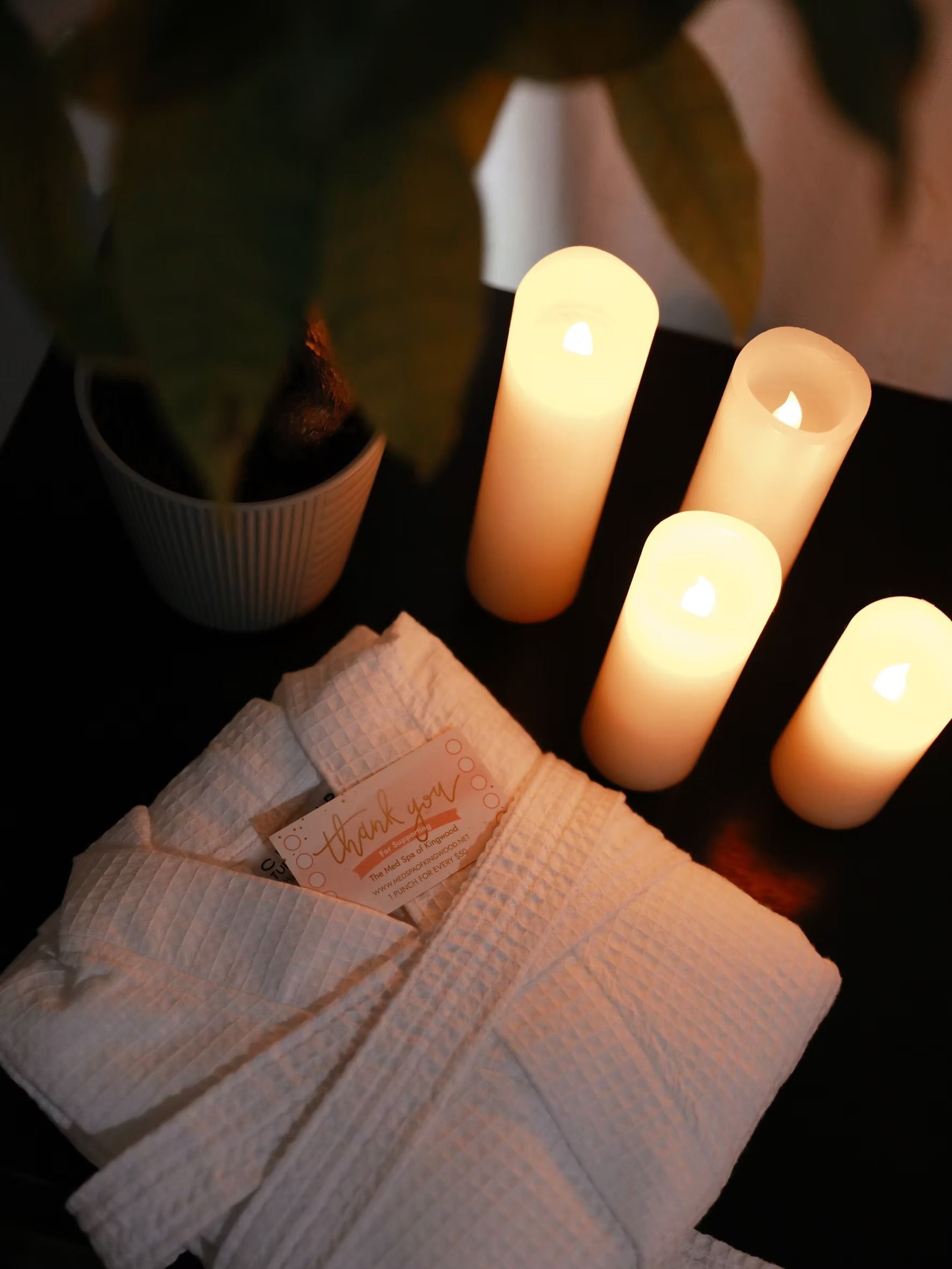 Folded white towels with lit candles on a dark table, creating a spa-like, warm atmosphere