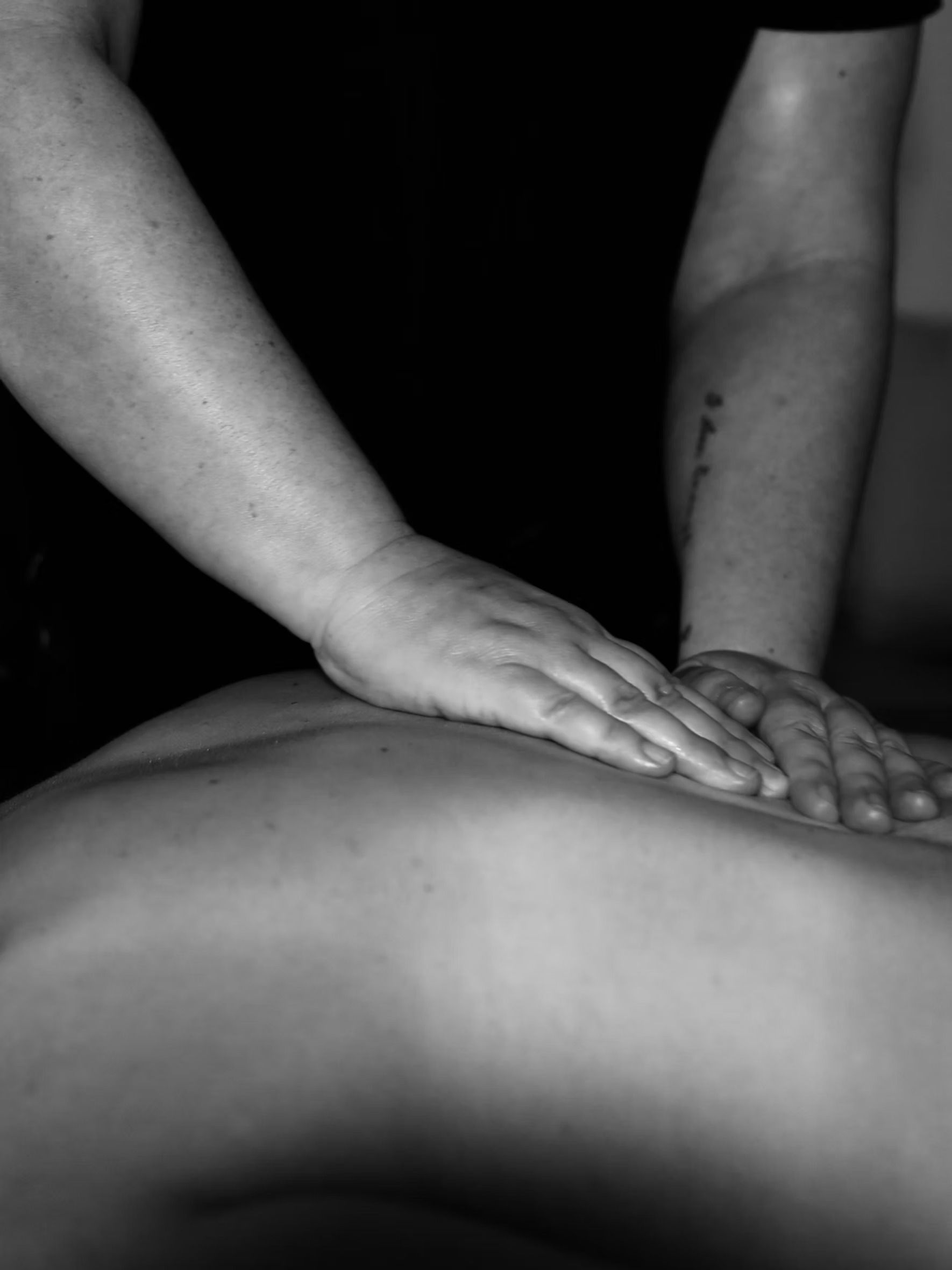 Two hands perform a massage on a person's back in black and white.