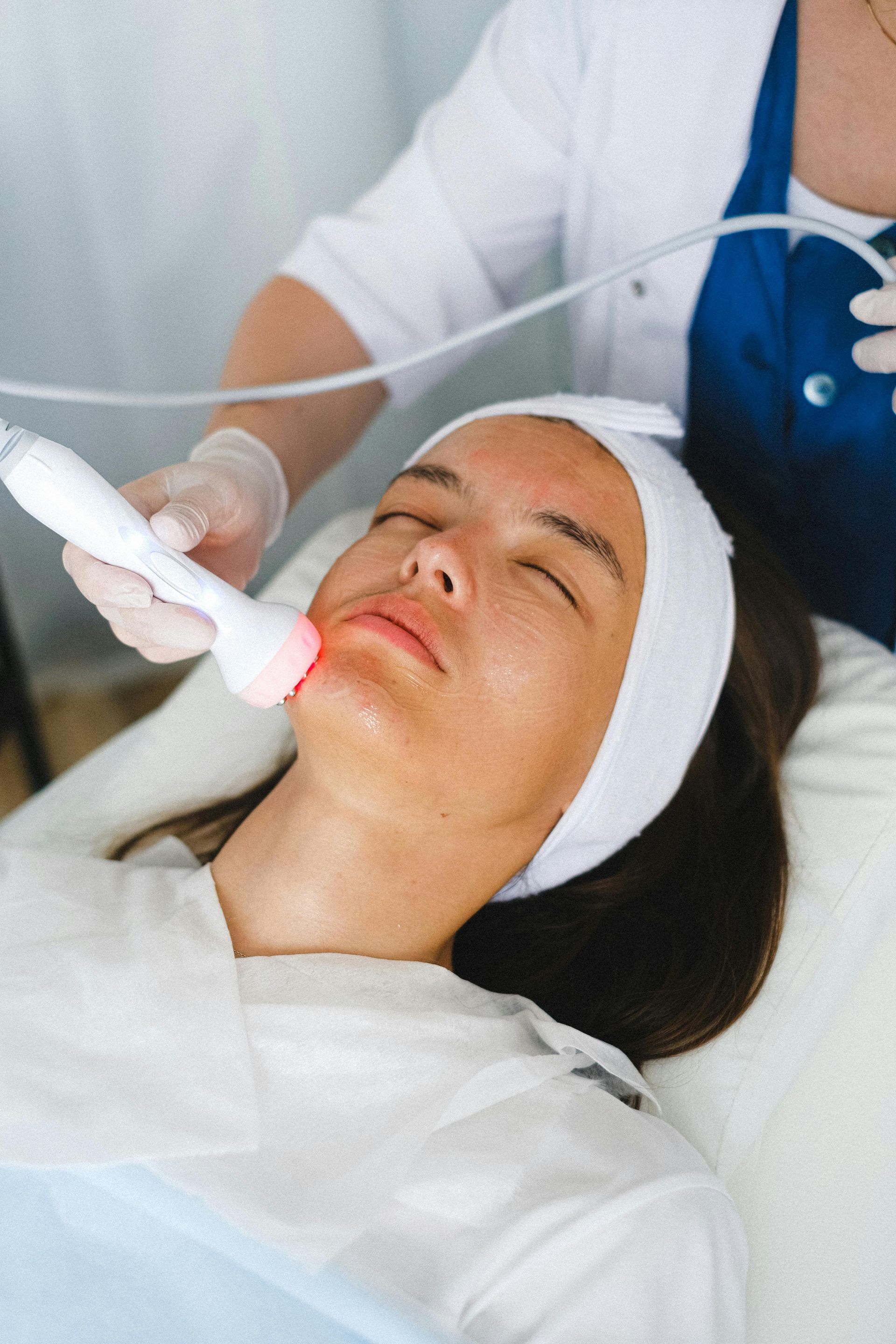 Person receiving a facial treatment with a handheld device while lying on a bed