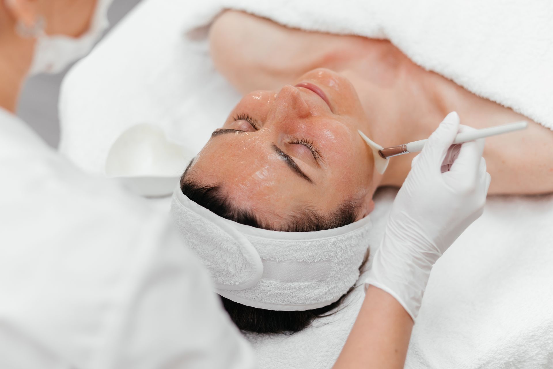 Woman receiving a facial treatment with a gloved hand applying product to her face in a spa setting