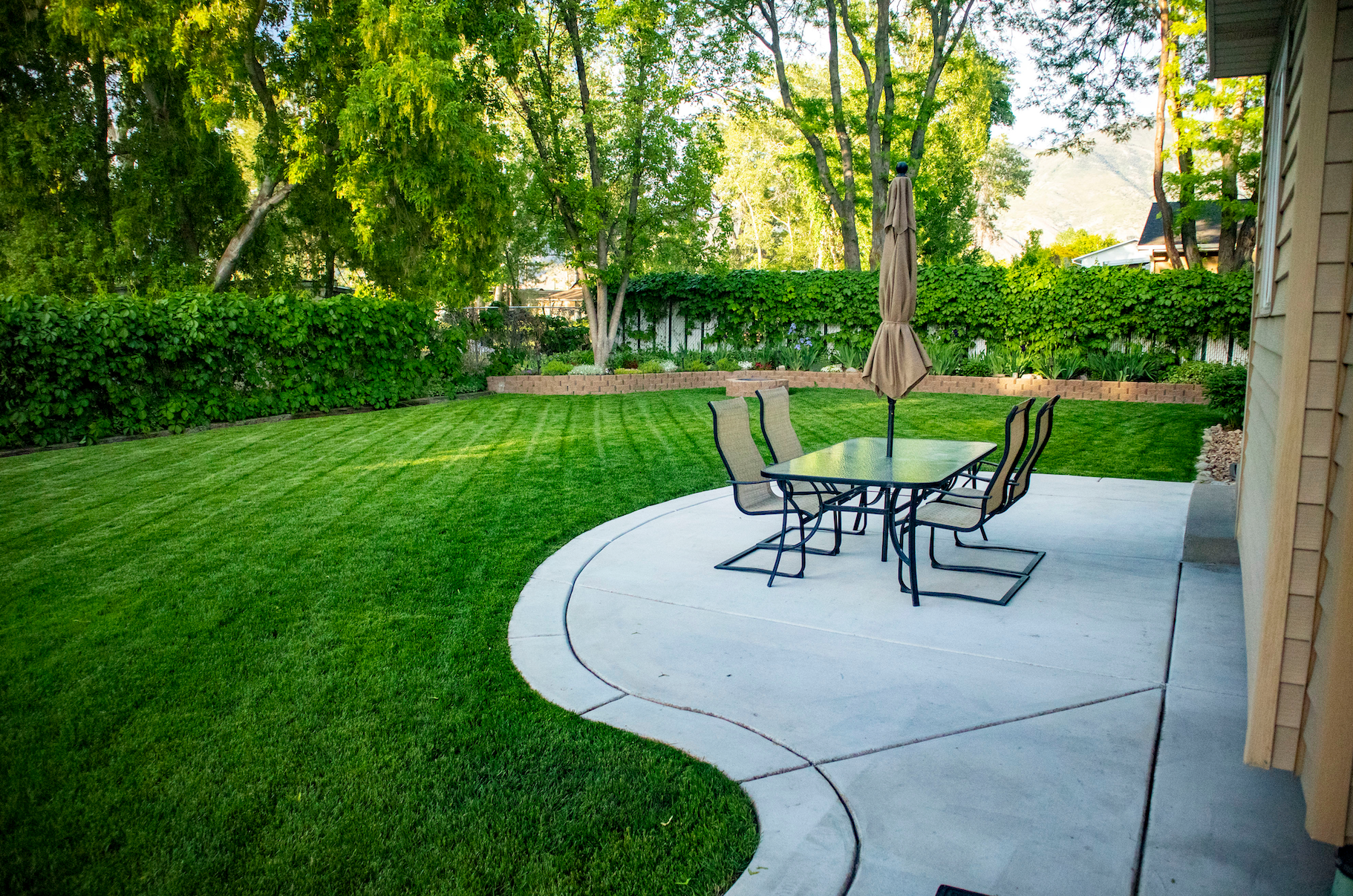 A patio with a table and chairs and umbrellas in a backyard.