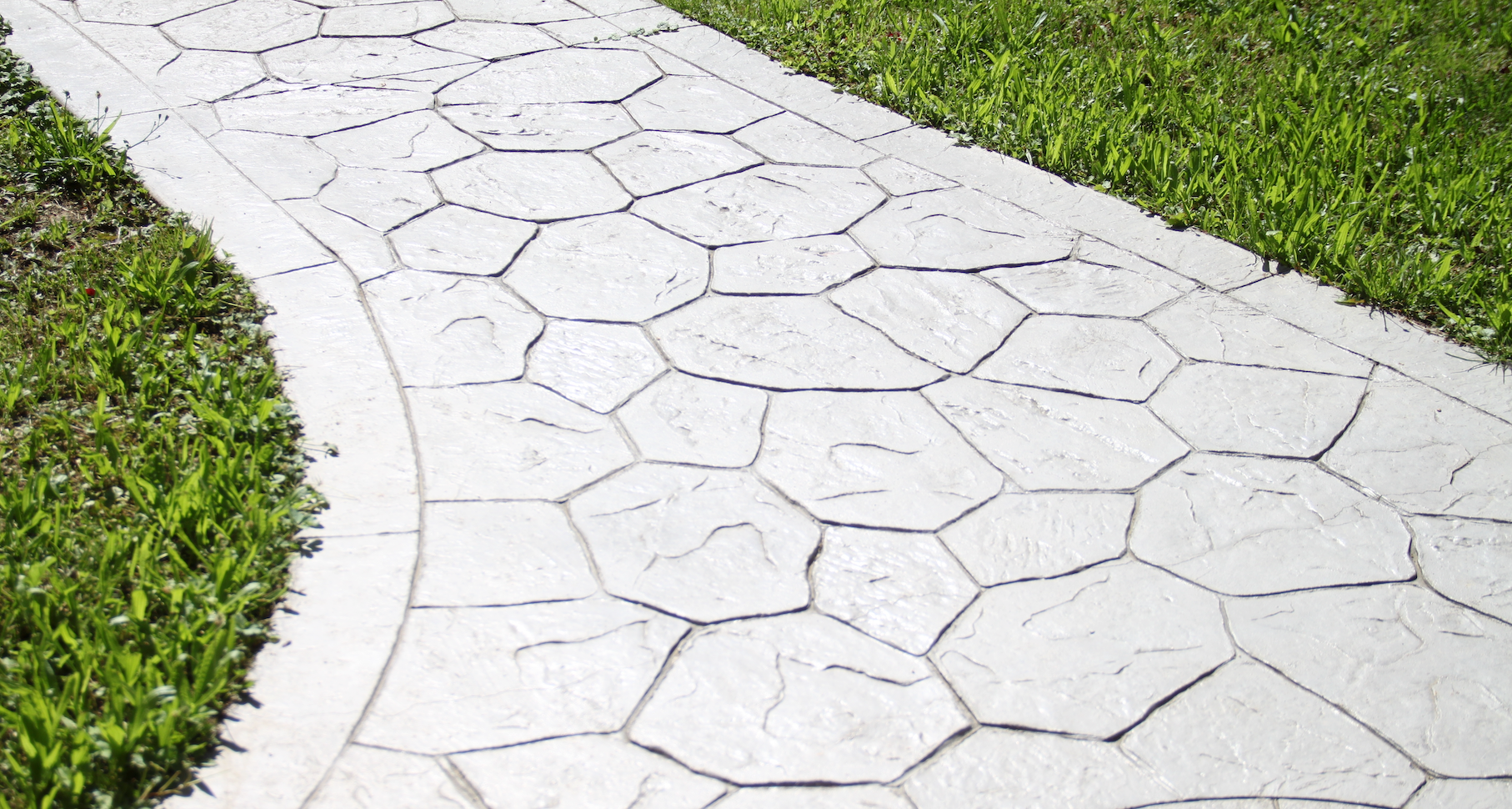 A white concrete walkway going through a grassy area.