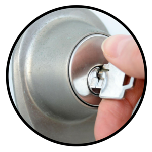 A hand inserts a silver key into a metallic door lock.