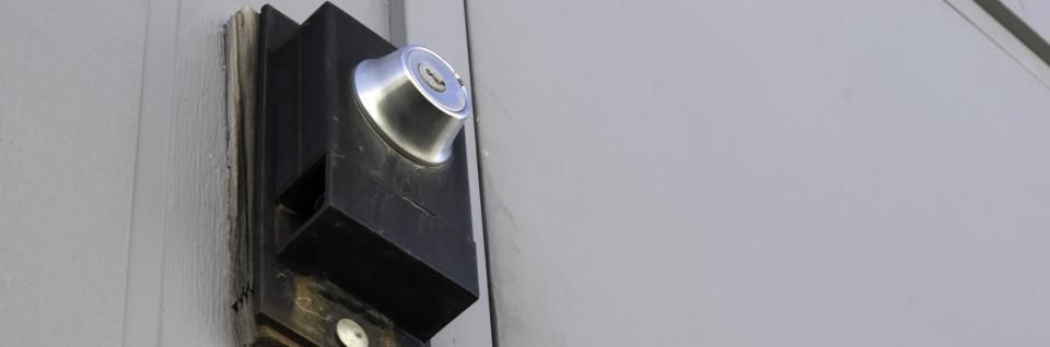 A black, rectangular lock box with a silver, circular key cylinder mounted on a plain, gray surface.