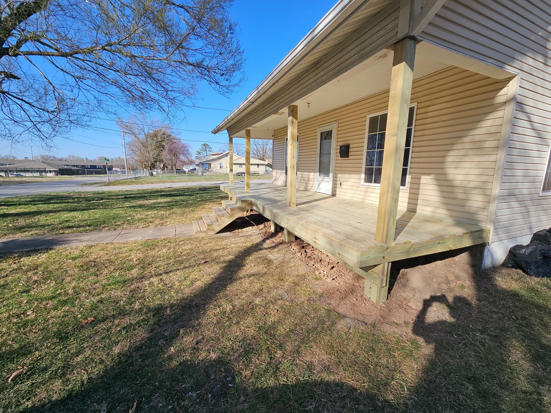 A house with a porch. The porch is supported by wooden posts. Brown grass and a blue sky.