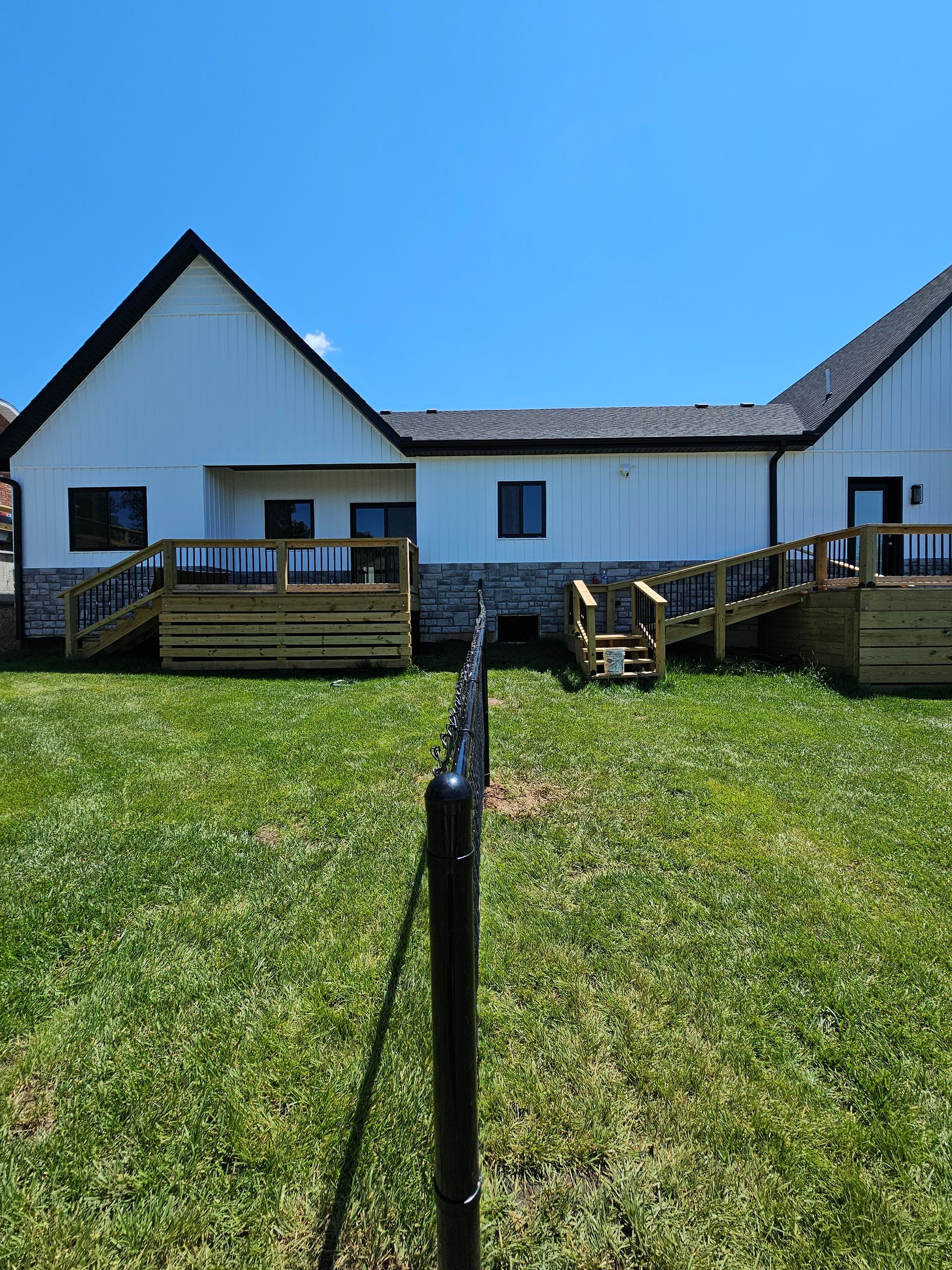 White building with wooden decks and stairs, set on a grassy lawn under a clear blue sky.