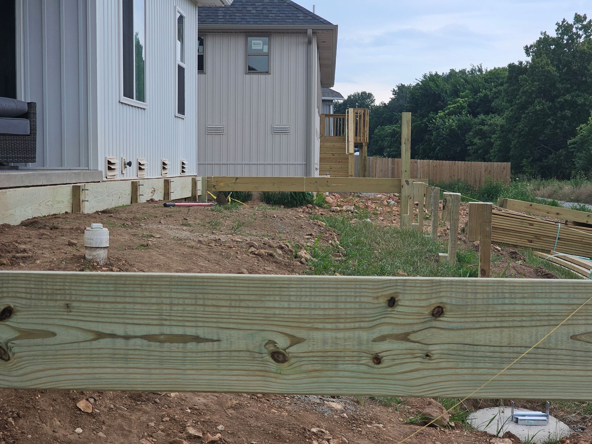 Construction site with a partially built deck near a white house.