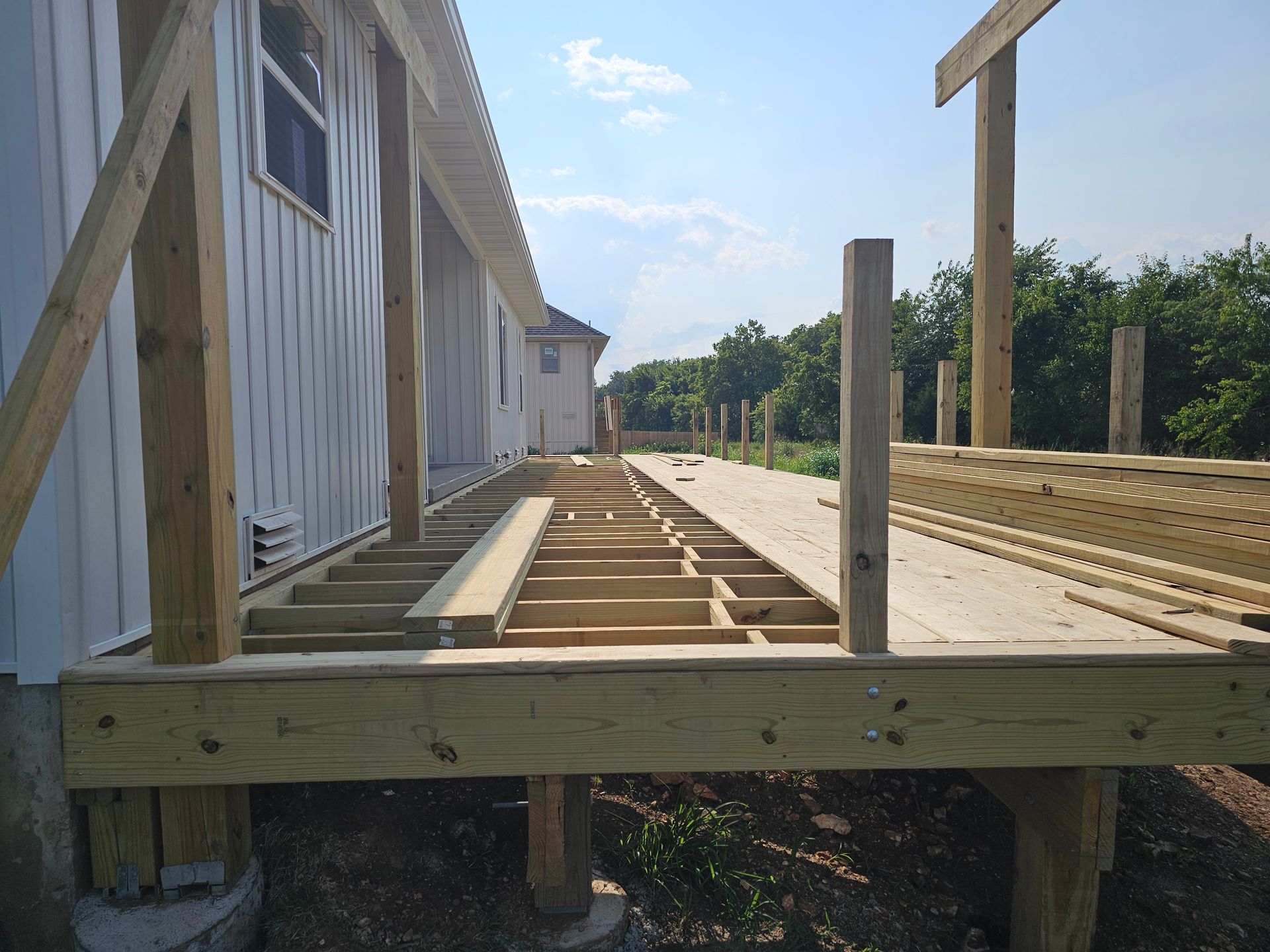 Wooden deck under construction next to a white house; framing and partial decking visible.