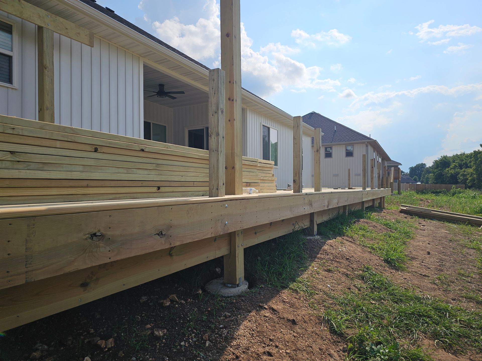Wooden deck under construction next to a white house, overlooking a grassy area.