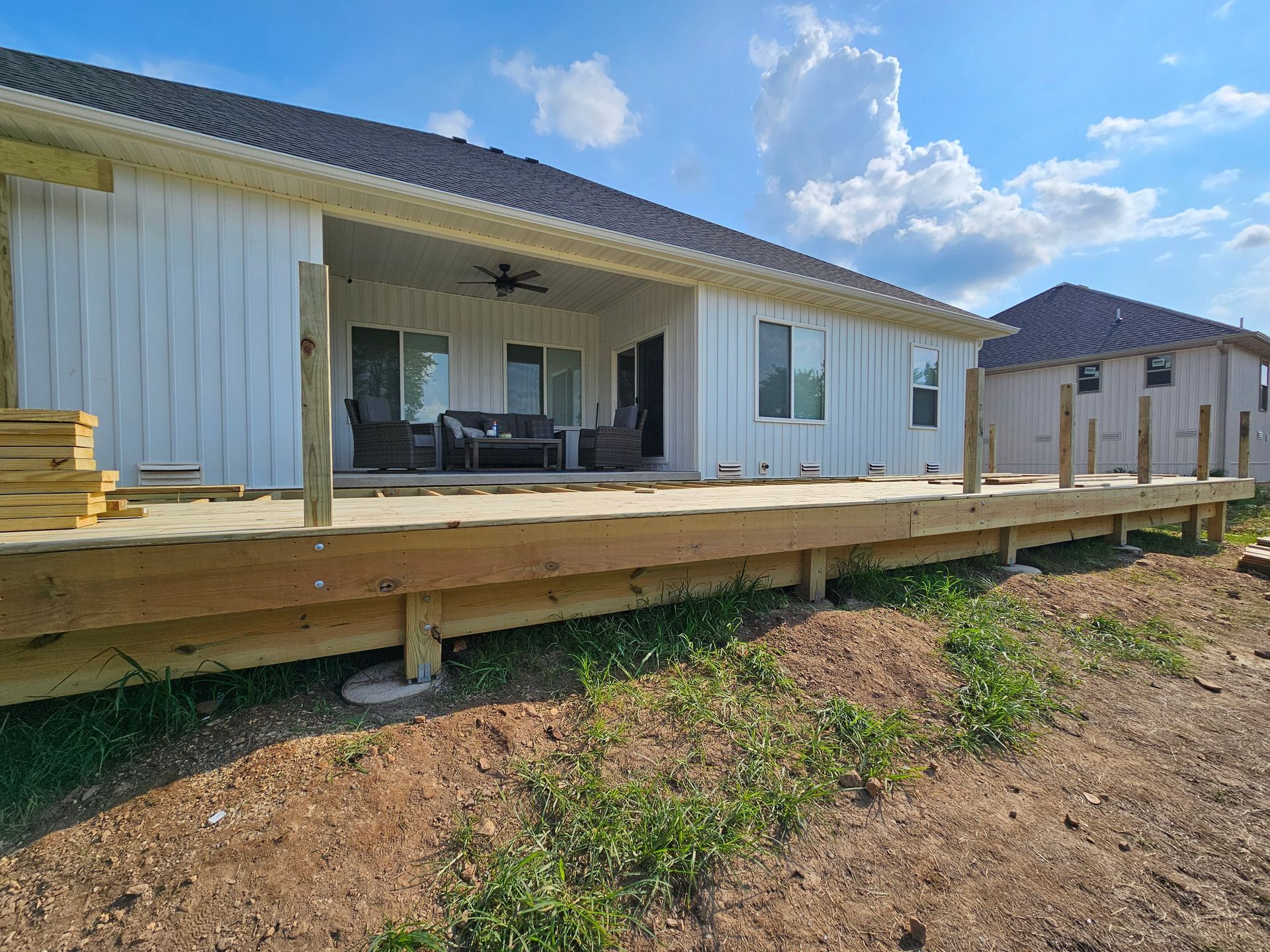 Wooden deck under construction next to a white house with a covered patio.