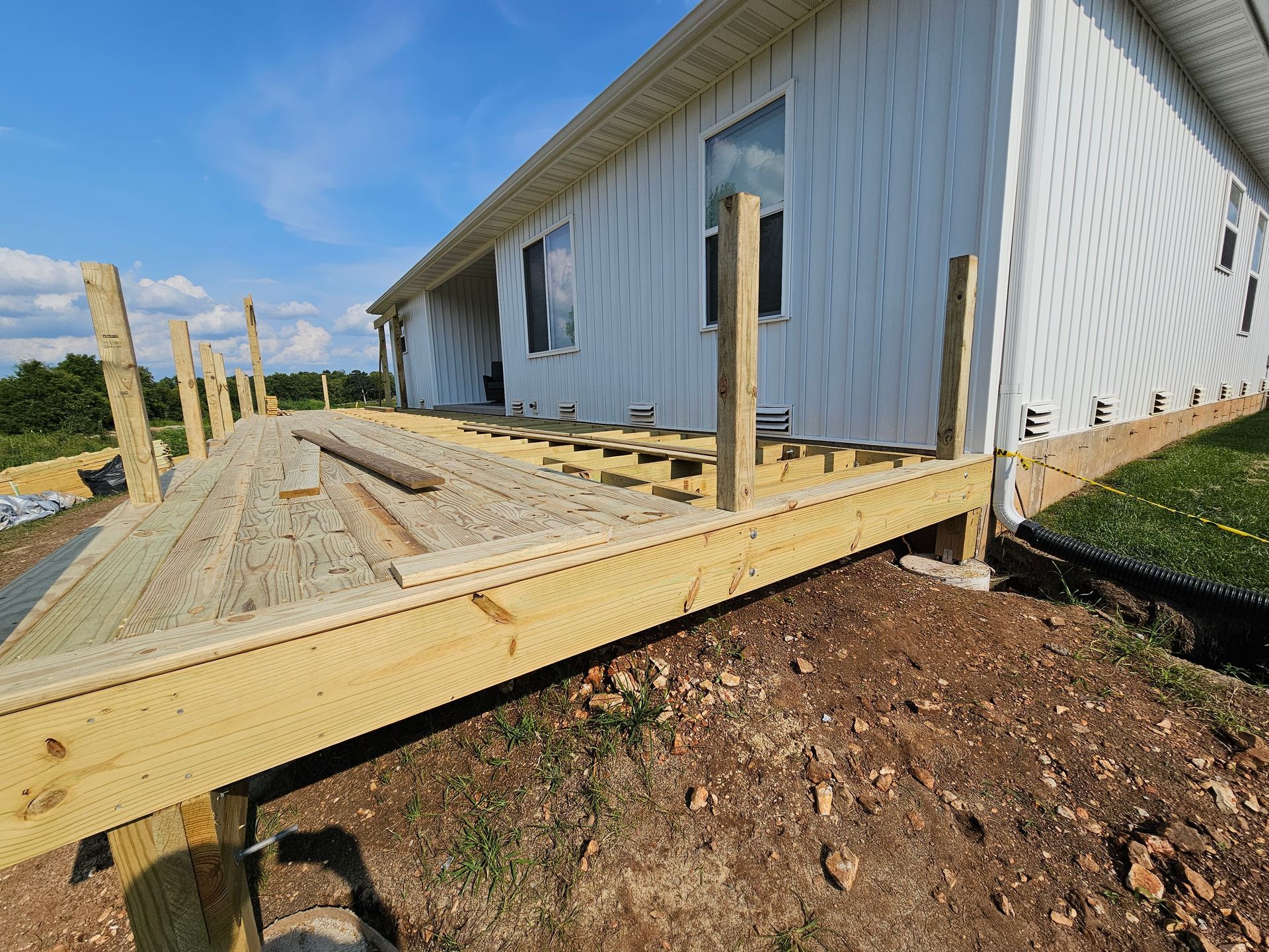 Newly constructed wooden deck attached to a white house, on a sunny day.