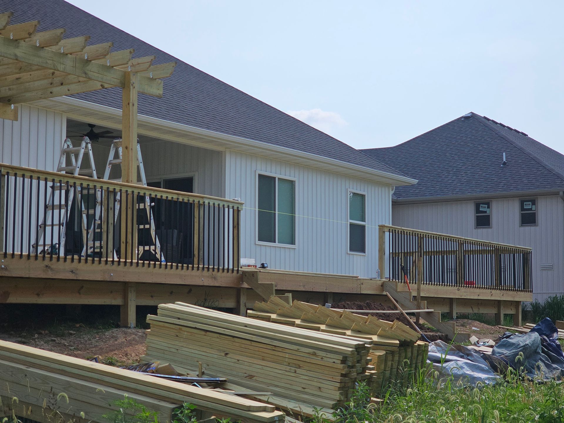 A partially built wooden deck attached to a white house with a dark roof; lumber and tools are visible.