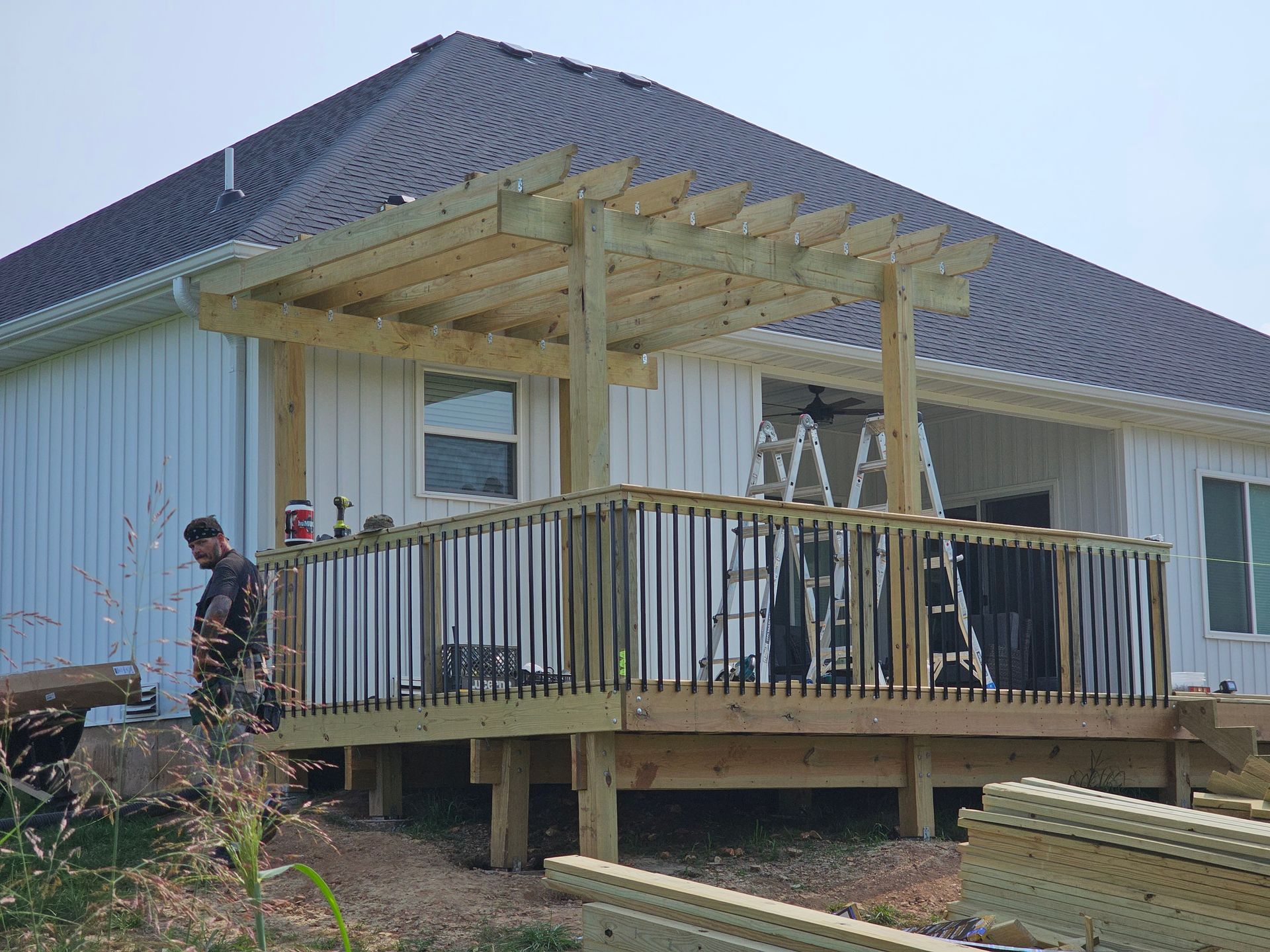 Wooden deck with pergola attached to a white house; a person stands near the deck.