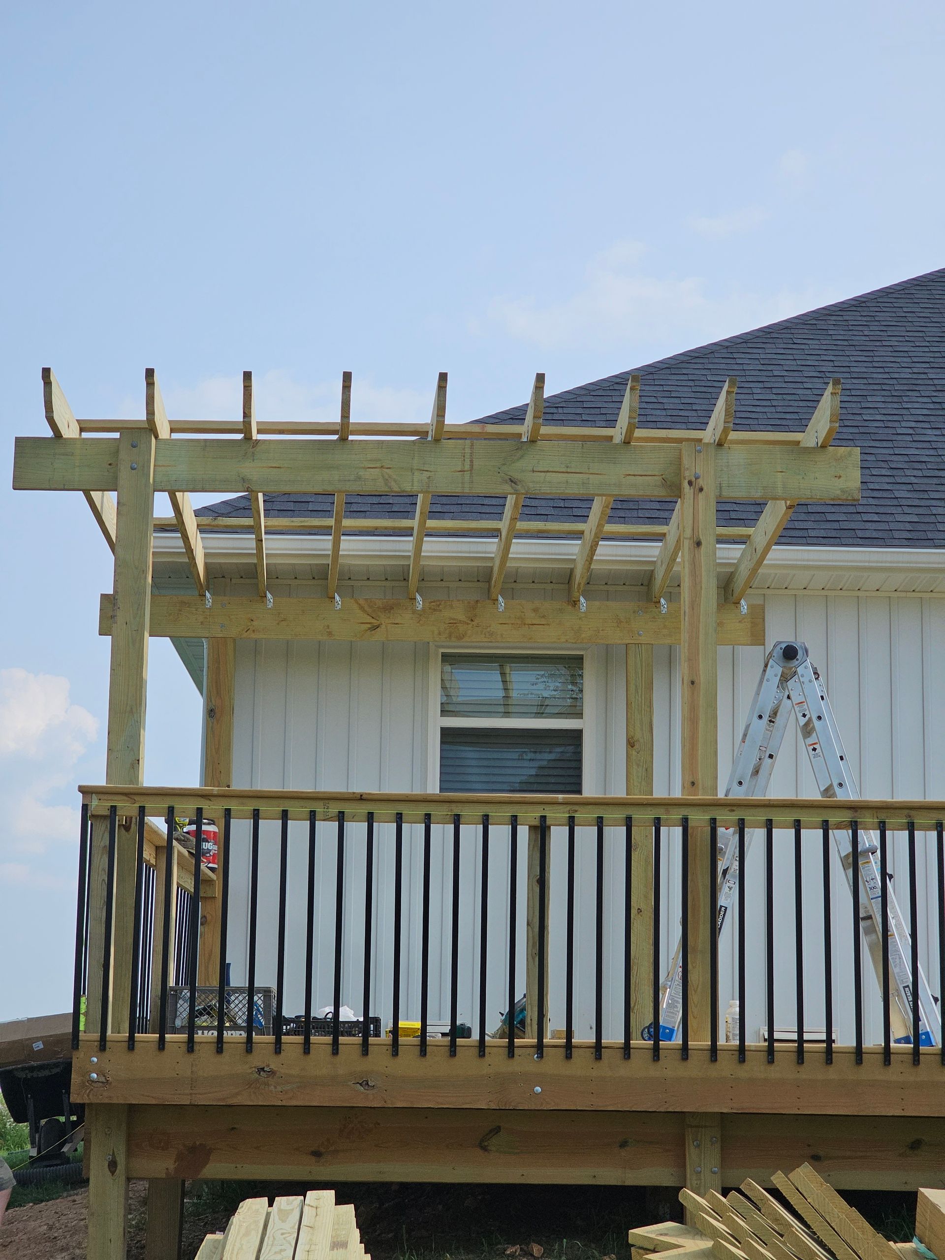 Deck with wooden railing and pergola against a white house and blue sky.