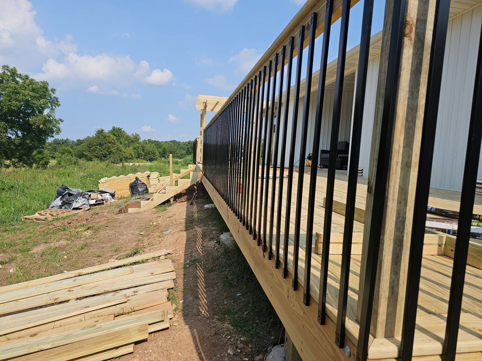 Wooden deck with black railing overlooking a field, construction materials visible.