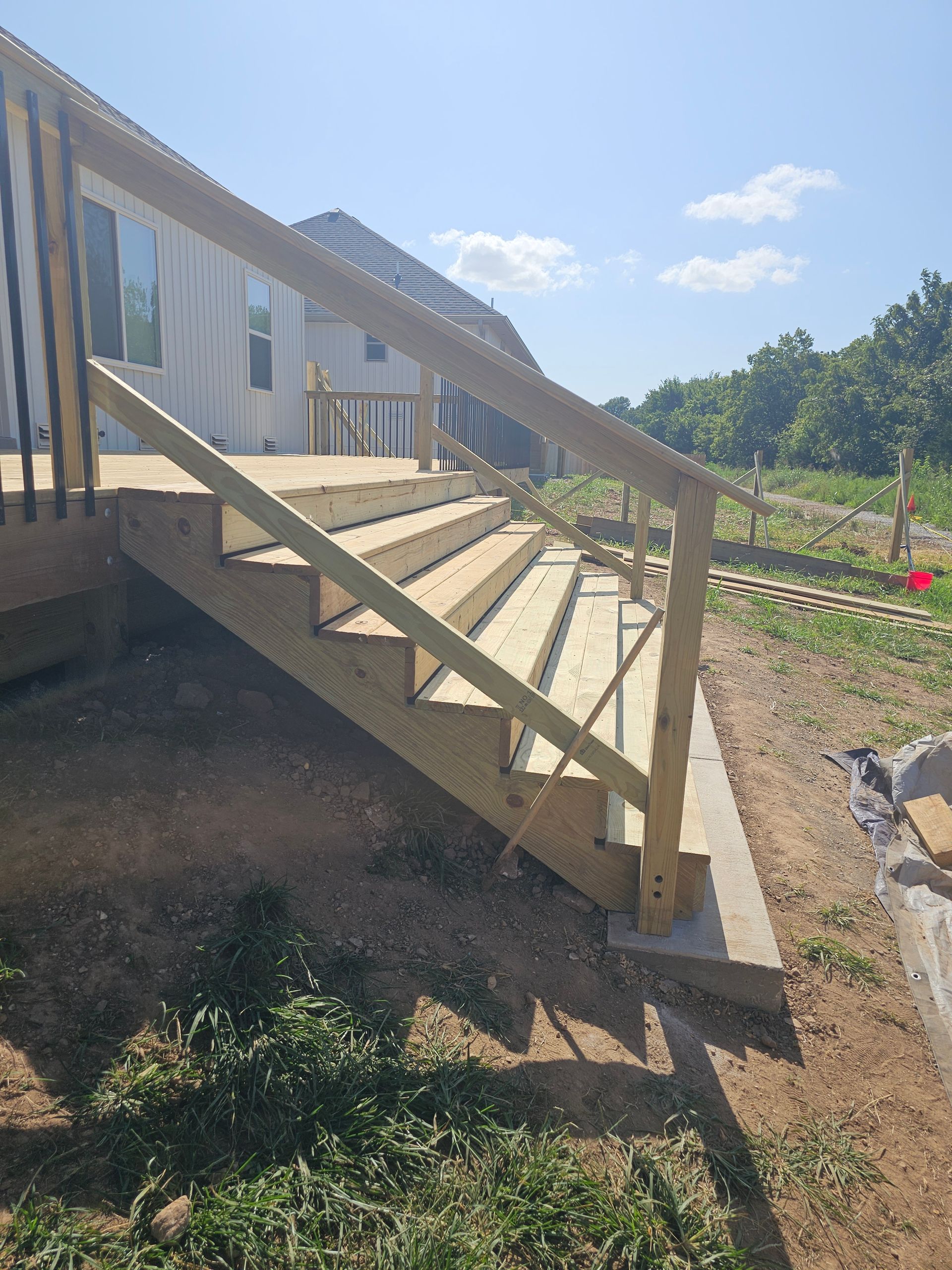 Wooden outdoor staircase with handrails leading down from a deck to the ground, sunny day.