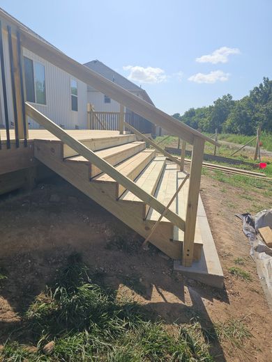 Wooden outdoor stairs with a handrail, leading down from a deck, on a sunny day.