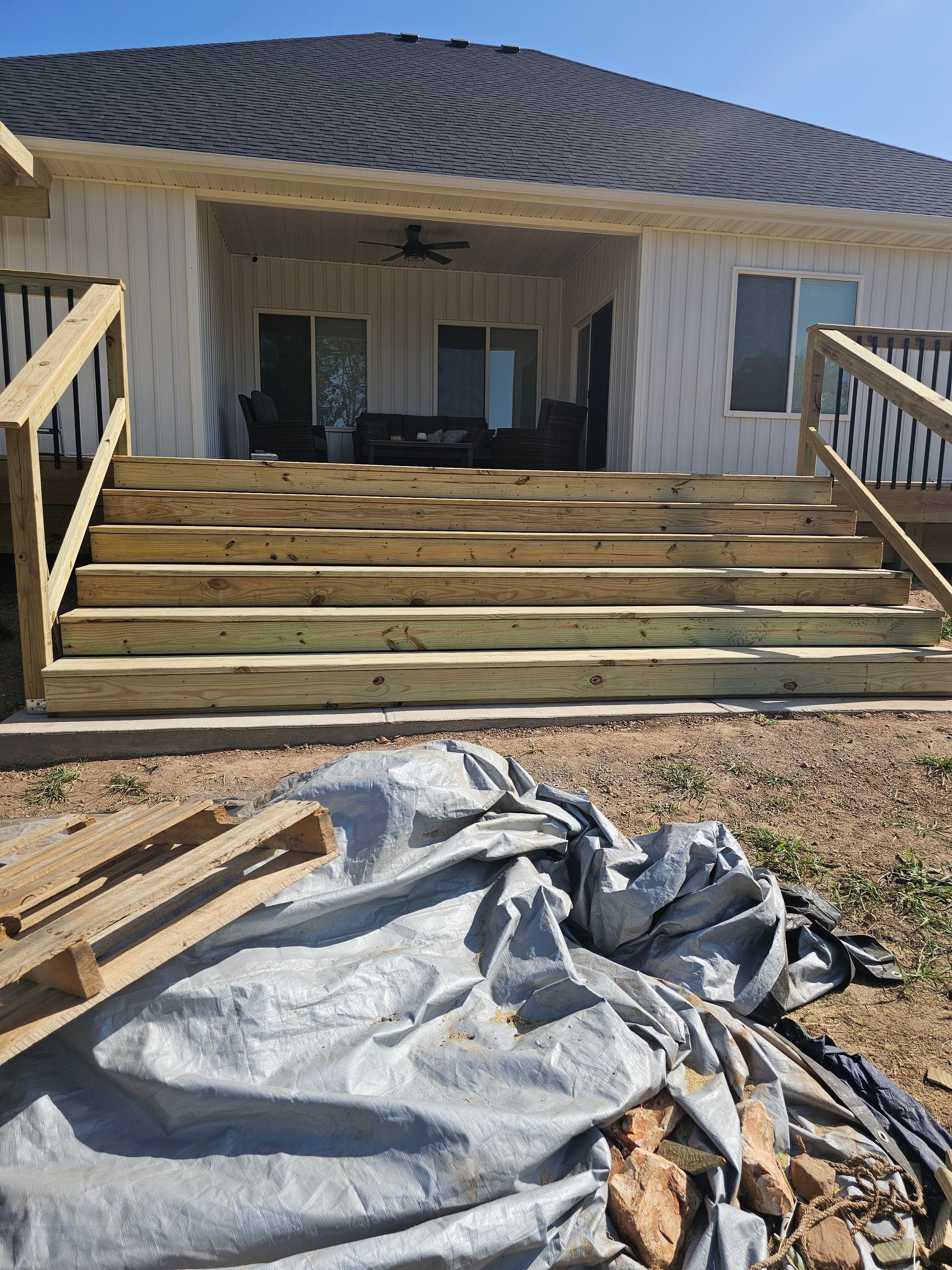 Wooden deck steps leading up to a house with a porch. Materials are in the foreground.