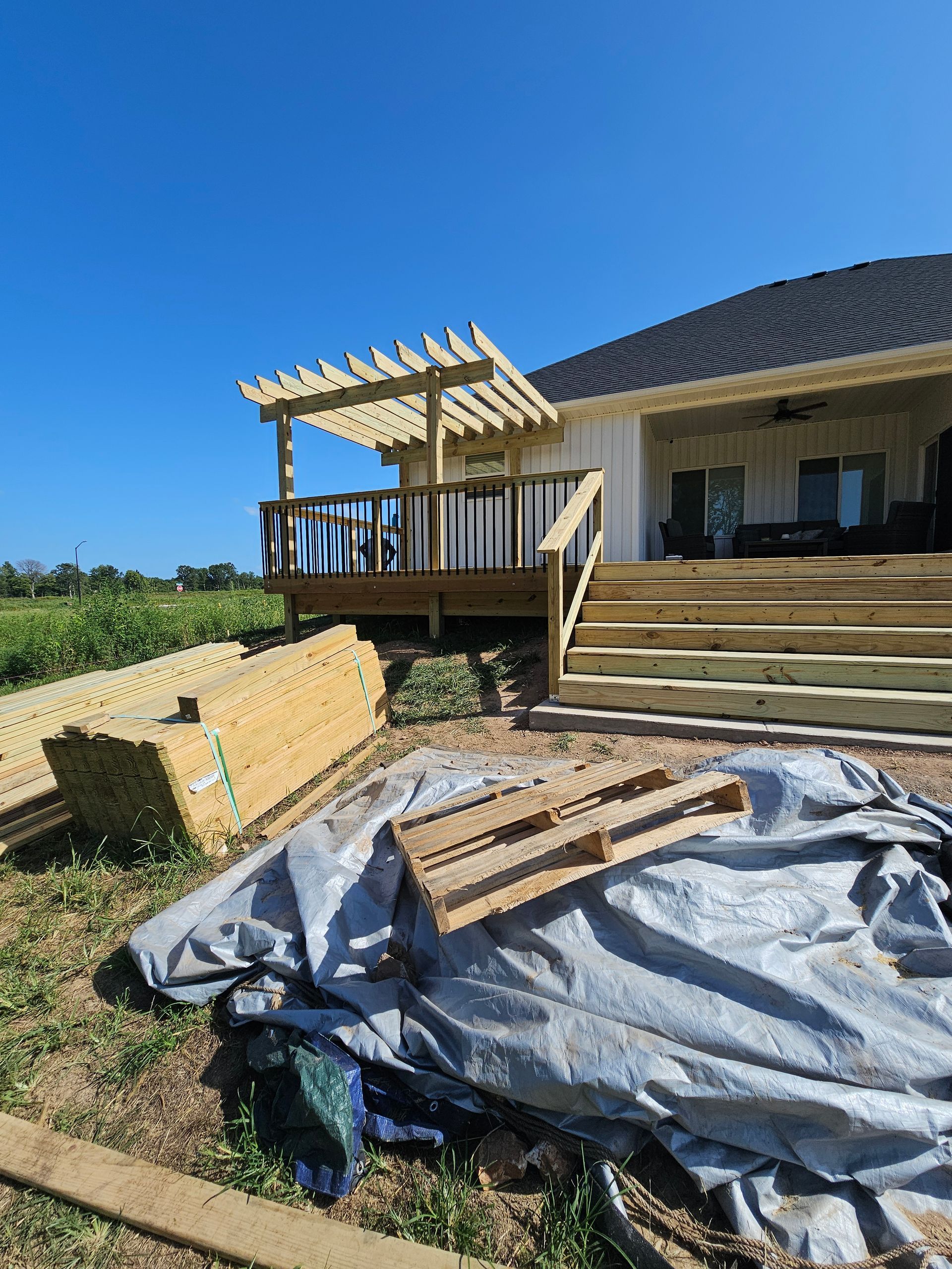 A newly built wooden deck with a pergola, steps, and lumber on a sunny day.