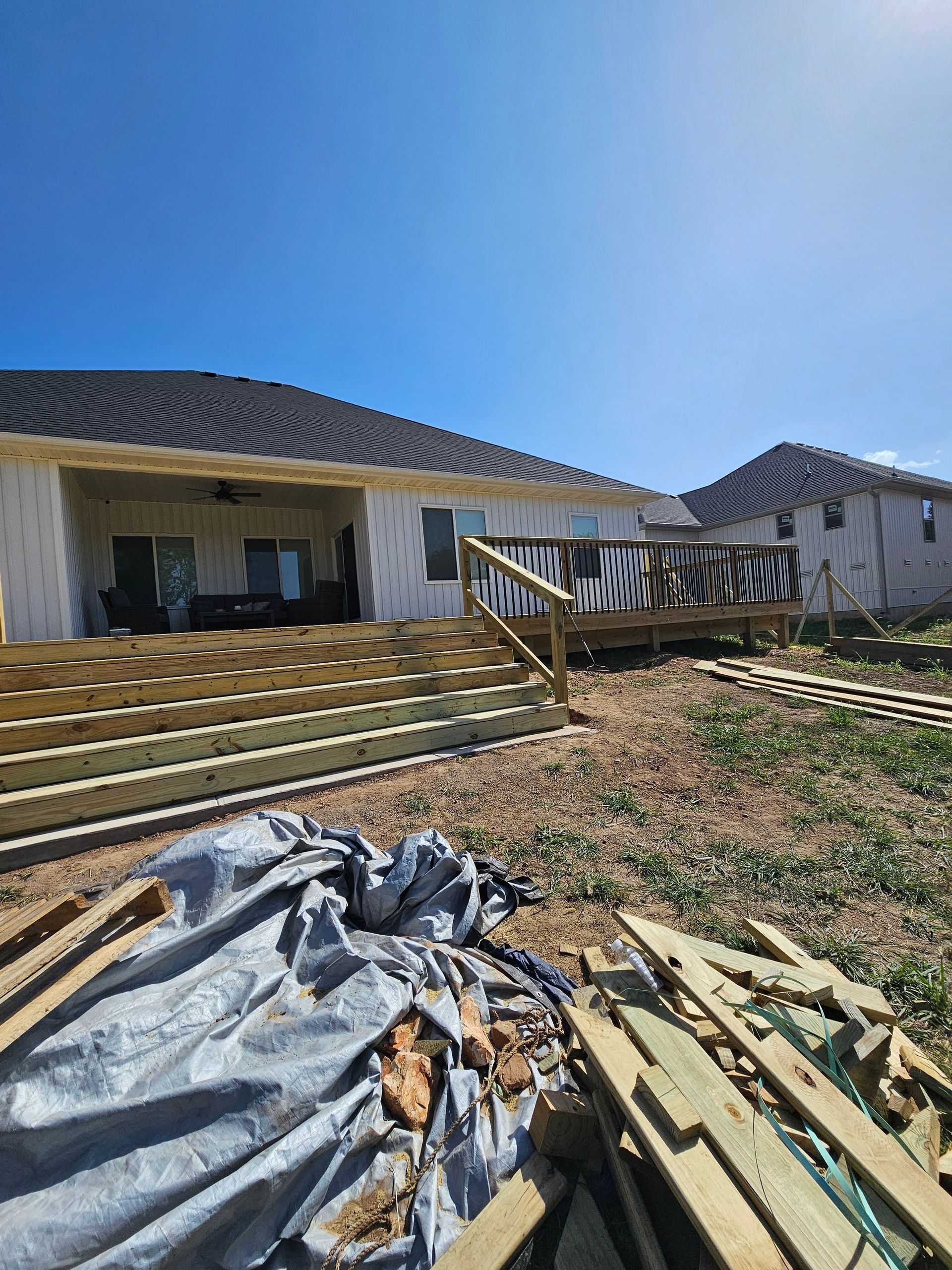 A partially built wooden deck with steps, connected to a house. Construction materials are scattered around.