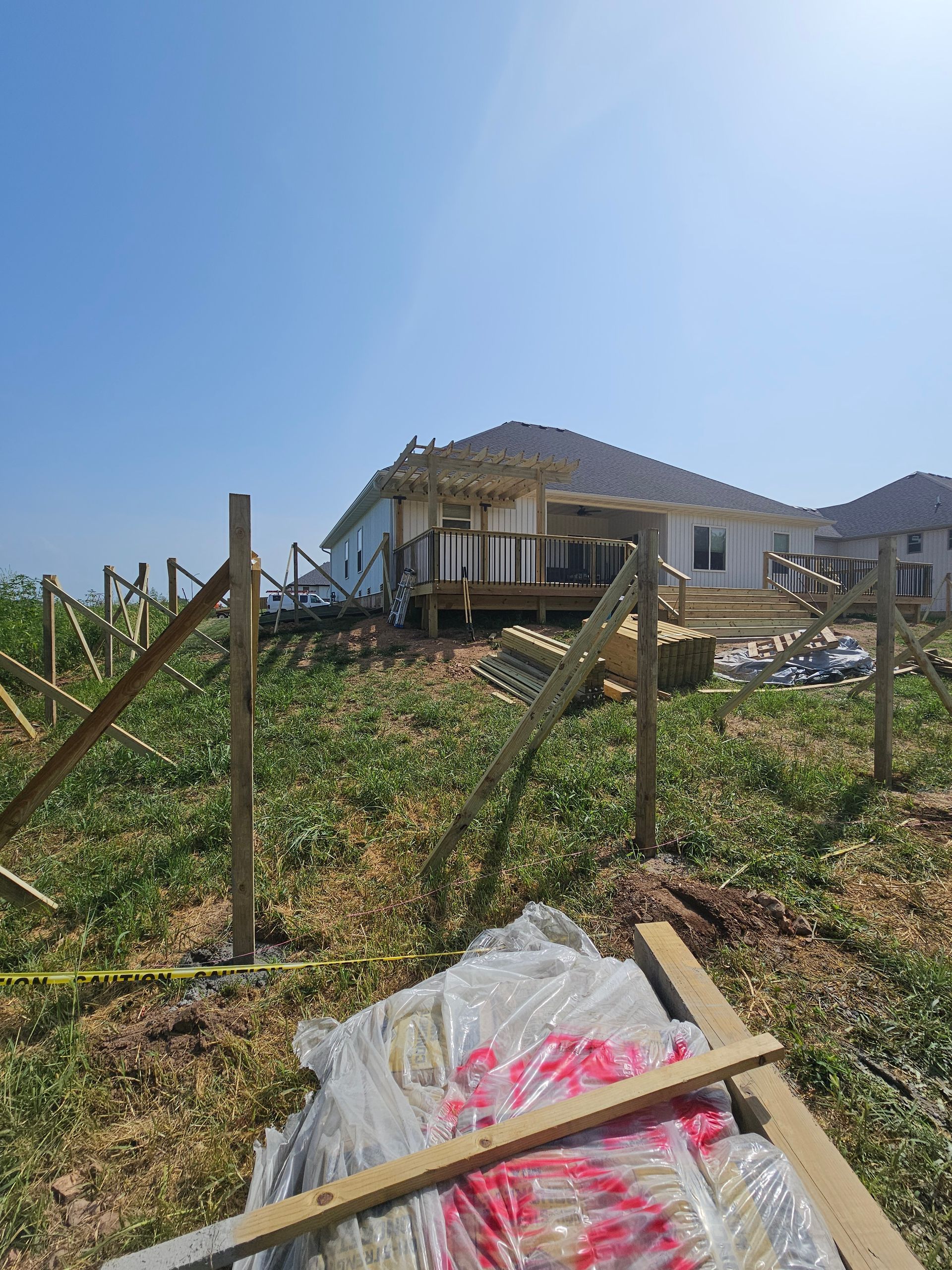 Construction of a wooden fence around a yard with a partially built deck on a house in the background.